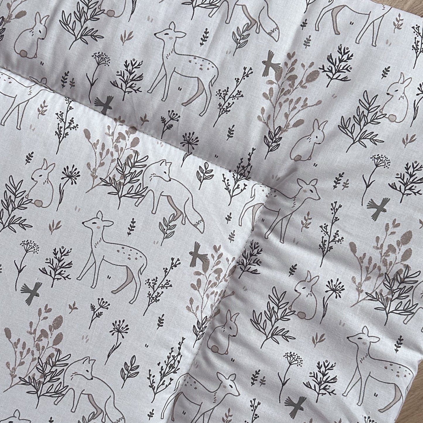 Detail van boxkleed Bas met een lieve print met hertjes, vosjes en konijntjes in het bos. Het dessin heeft zachte tinten beige en grijs op een witte ondergrond.
