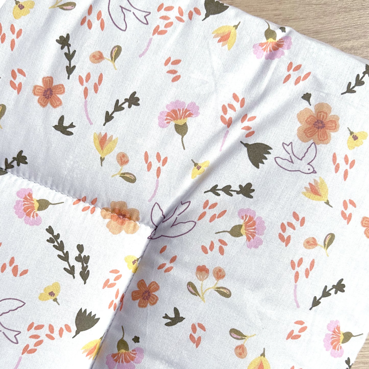 Detail van boxkleed Saar met vrolijke bloemen en vogels in roze, oranje, geel en groen op een witgrijze ondergrond.