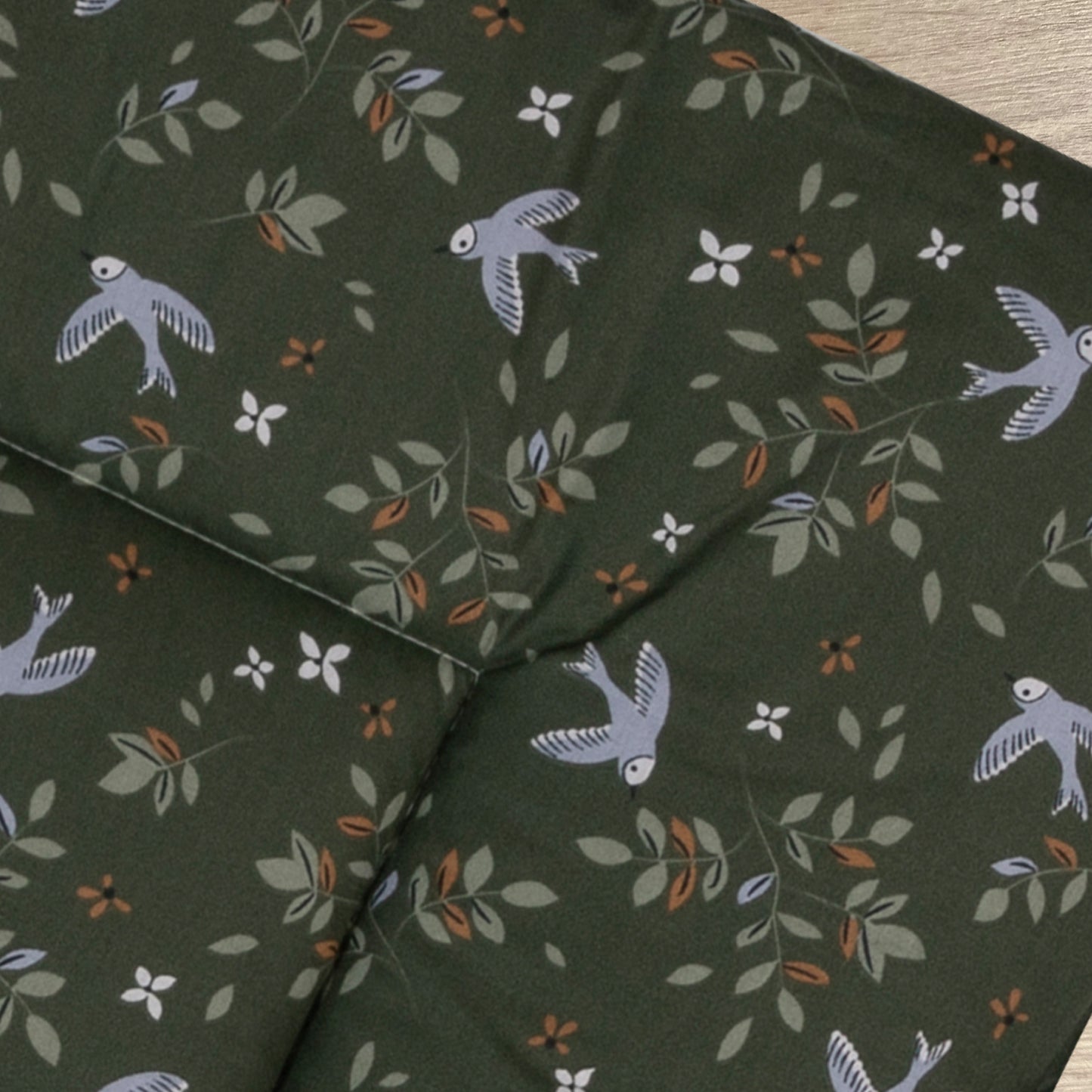 Detail van boxkleed Merel met een mooie print van bloemen en vogels in lila, licht groen en camel op een donkergroene ondergrond.