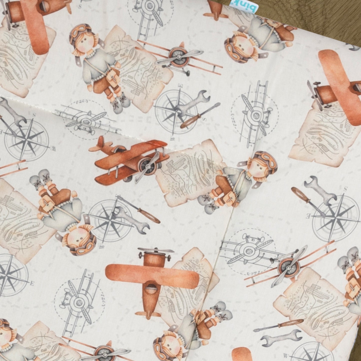 Detail van boxkleed Raf heeft een vrolijke print met vliegtuigen en een handige piloot die de wereld gaat ontdekken. Een fijn boxkleed in zachte tinten zoals terra, oranje, bruin, grijs, beige op een ecru ondergrond