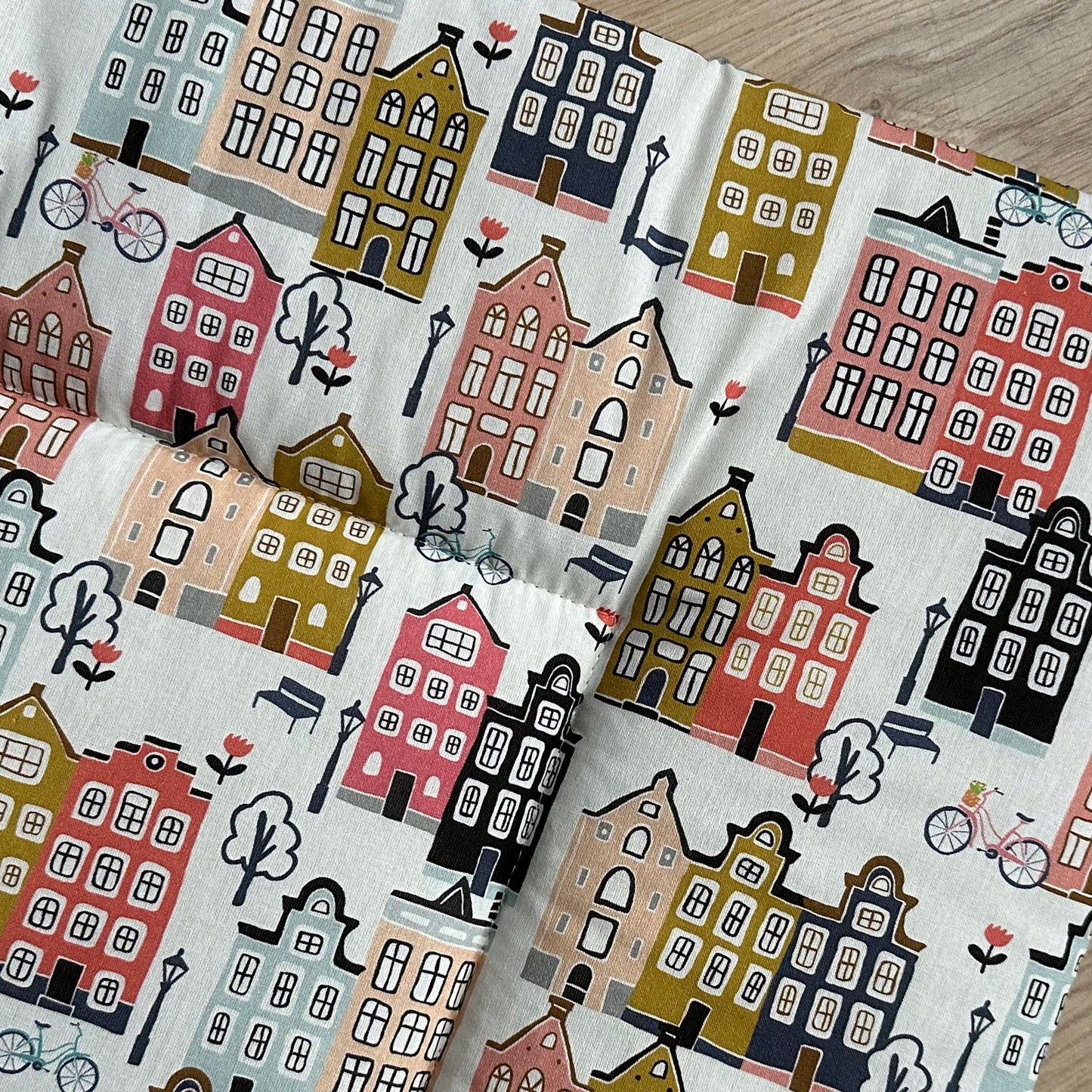 Detail van boxkleed Adam met een vrolijke print met grachten huisjes in mooie tinten zoals peach, roze, bleu, grijs en mosterdgeel op een ecru ondergrond.