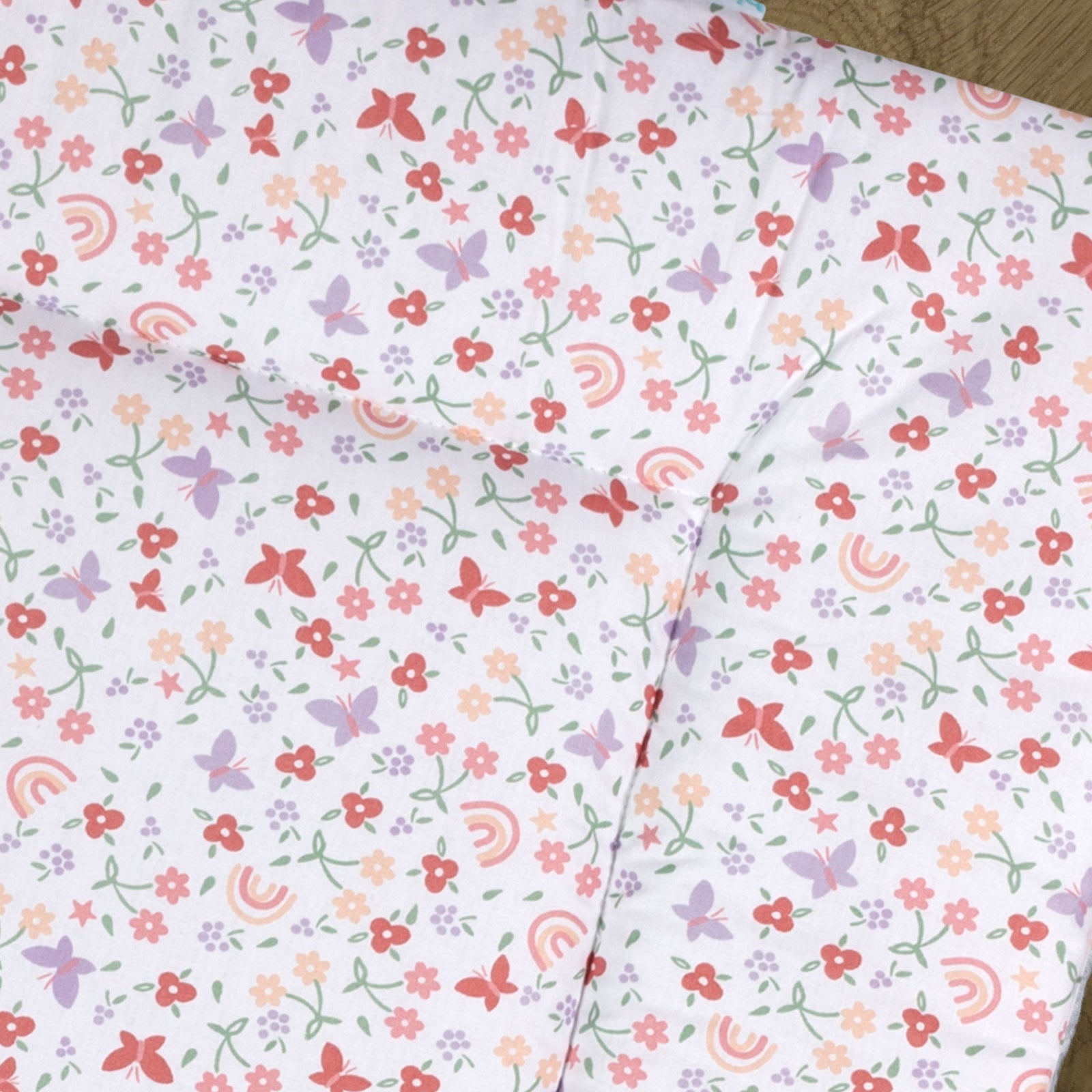 Detail van boxkleed Linde met een vrolijke print vol bloemen, vlinders en regenbogen in zachte tinten zoals lila, roze, groen en peach op een witte ondergrond. 