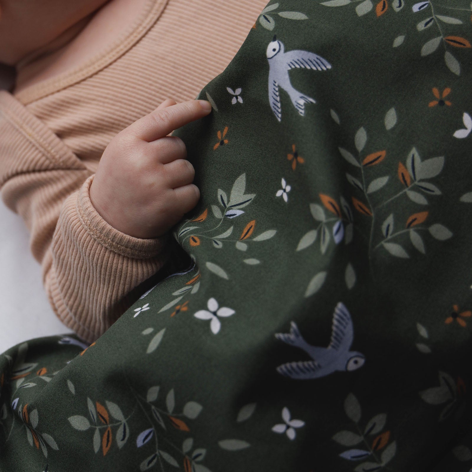 Sfeerbeeld met handje Binck van dekbedovertrek Merel met een mooie print met vogels, bloemen en takken met bladeren in lichtgroene tinten, caramel bloemen en lila accenten.